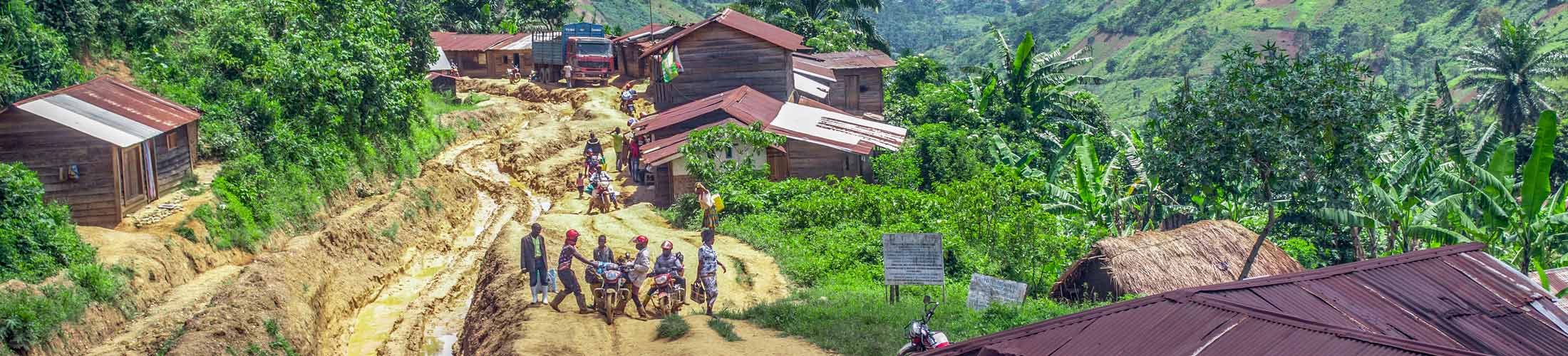A rural village with wooden houses and a muddy road with people on the go