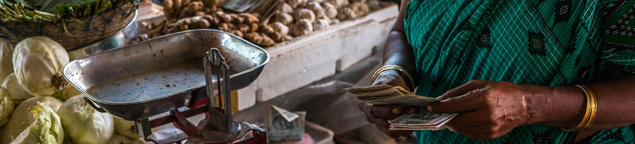 A woman counting money at a fruit and vegetable stand